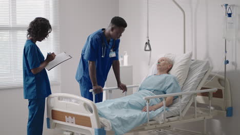 Senior-patient-on-bed-talking-to-2-African-American-doctor-in-hospital-room-Health-care-and-insurance-concept.-Doctor-comforting-elderly-patient-in-hospital-bed-or-counsel-diagnosis-health.